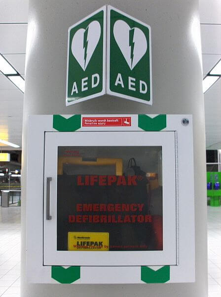 Kasten am Flughafen mit Laien-Defibrillator und grüner Hinweistafel mit "AED"